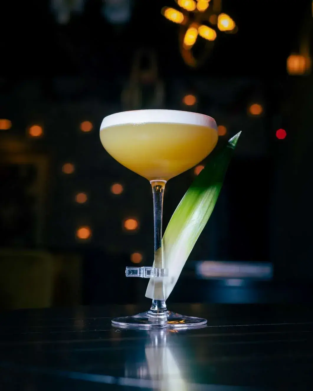 Golden coupe cocktail with a foam cap and pineapple leaf, candlelit wall behind
