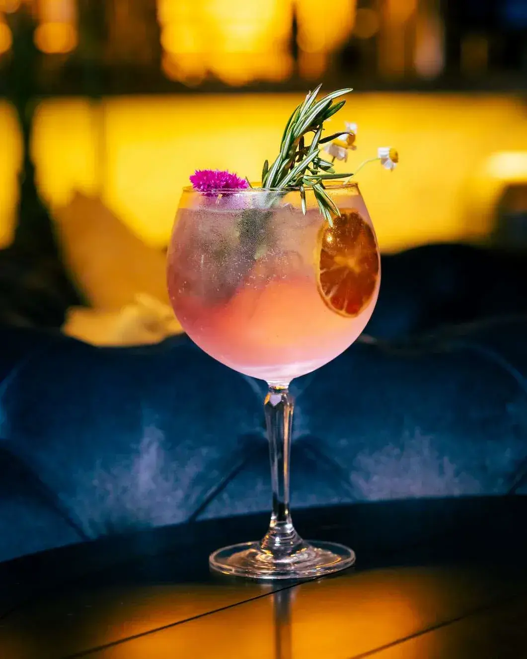 Pink gin and tonic in a balloon glass with rosemary, chamomile and dried lime