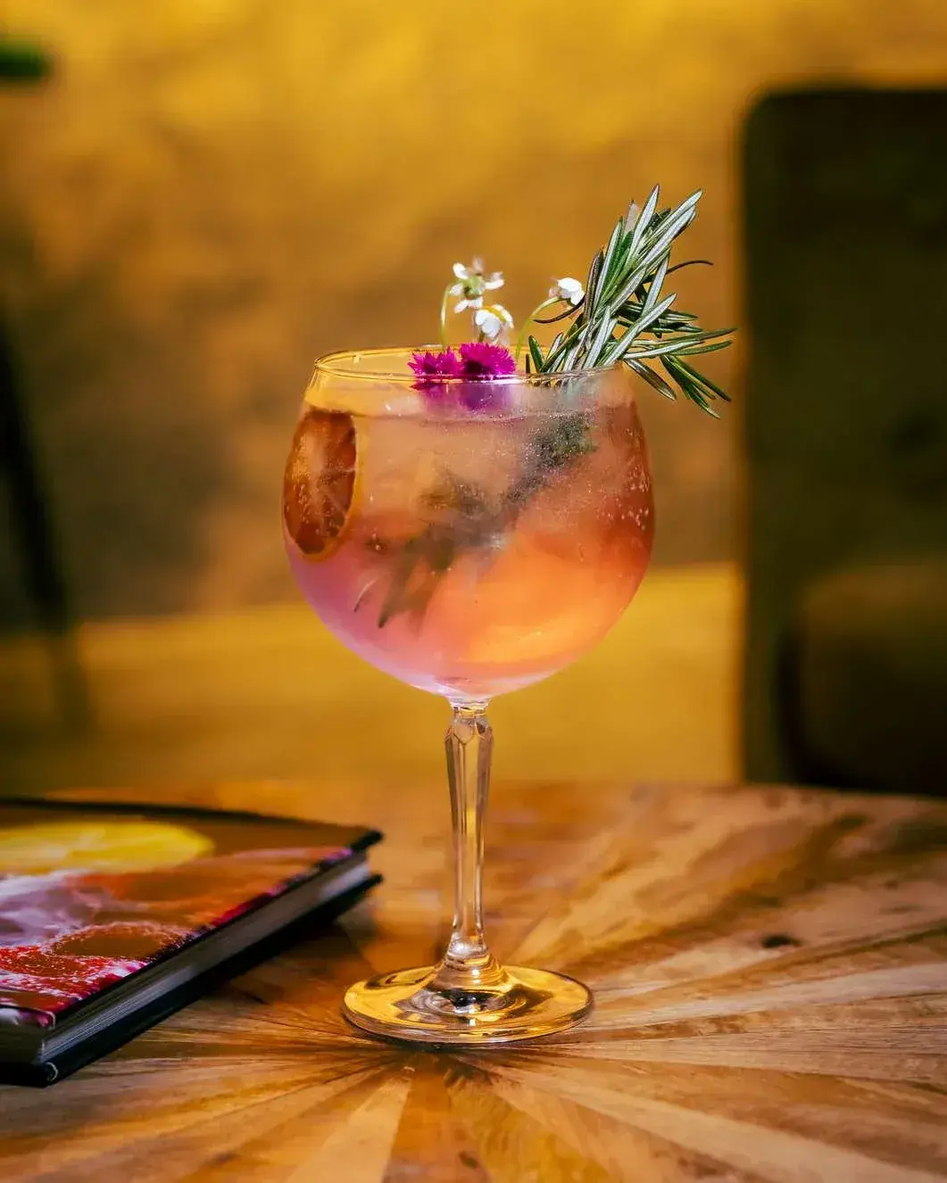 Balloon glass gin and tonic with edible flowers against a warm gold wall