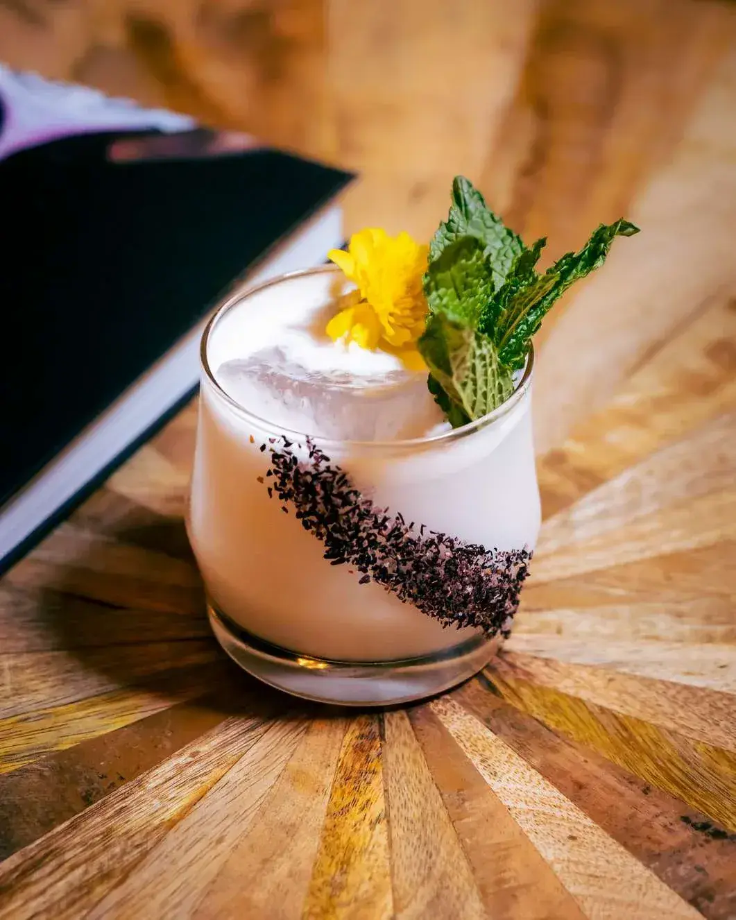 Creamy rocks cocktail with a diagonal cacao rim, mint and a yellow flower