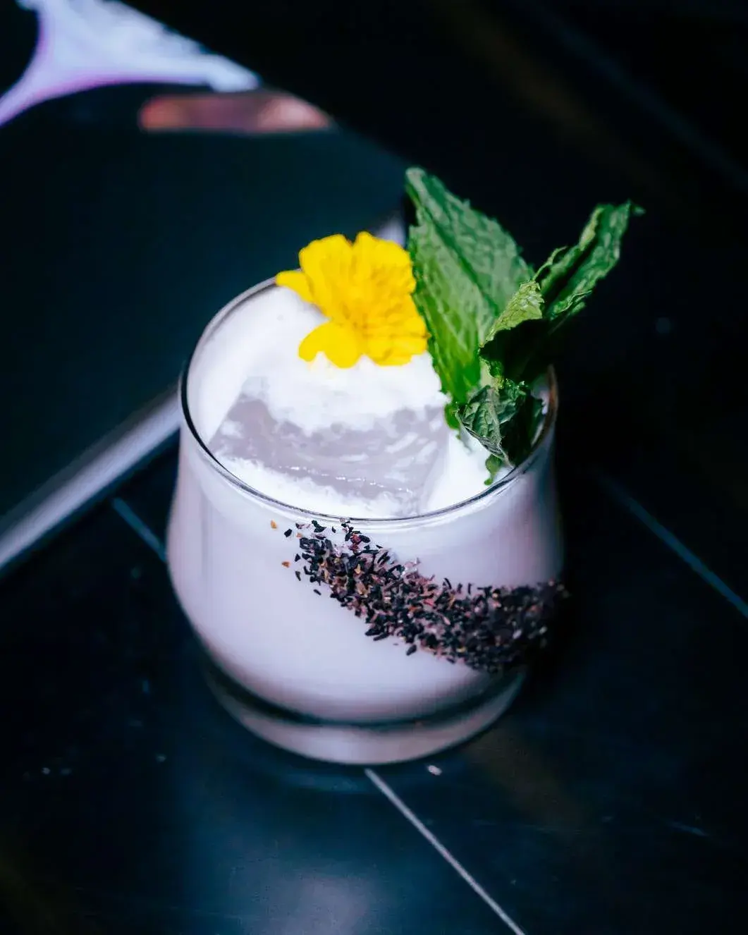 Creamy cocktail with a cacao stripe and marigold garnish on a black table
