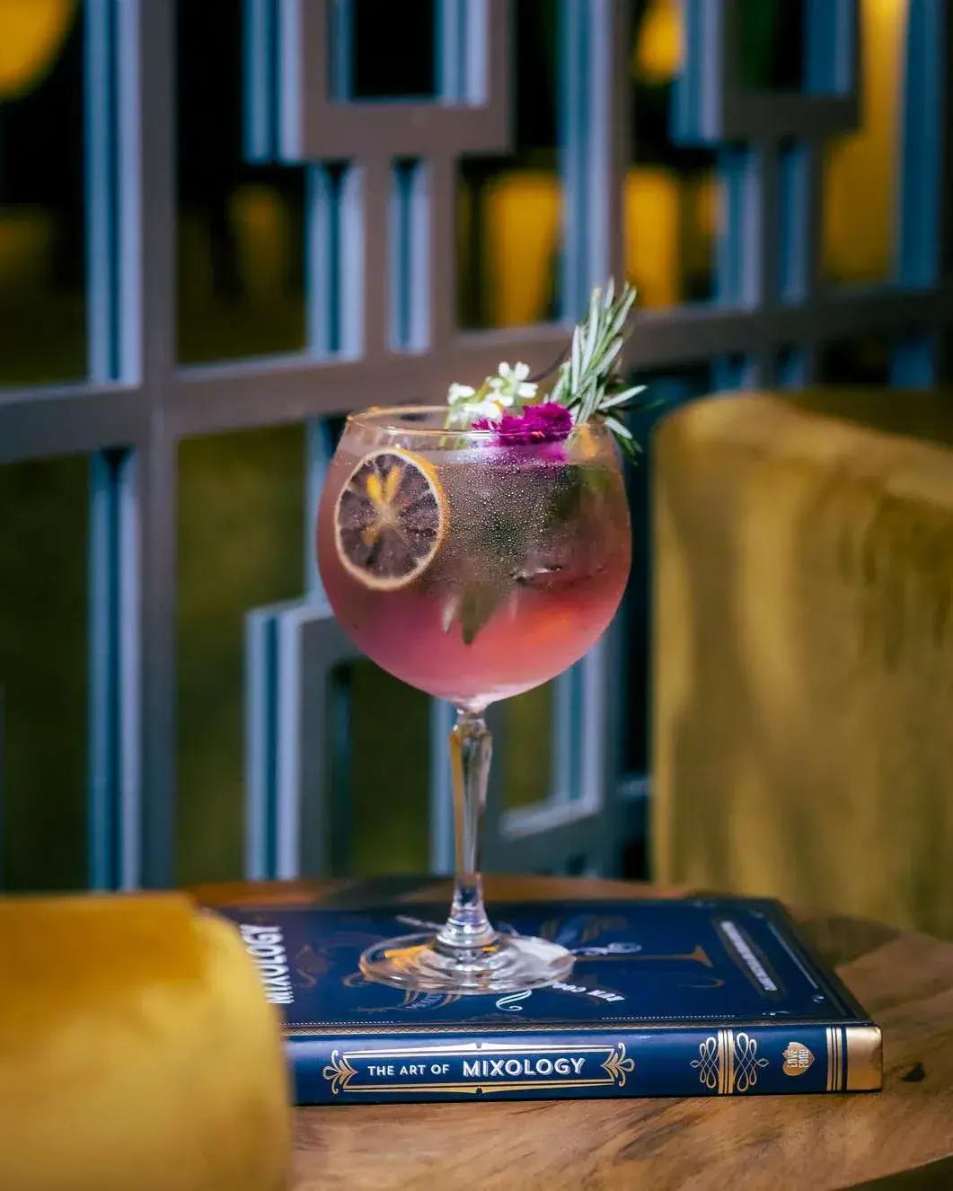 Balloon cocktail with a dried lime wheel and rosemary, teal lattice screen behind