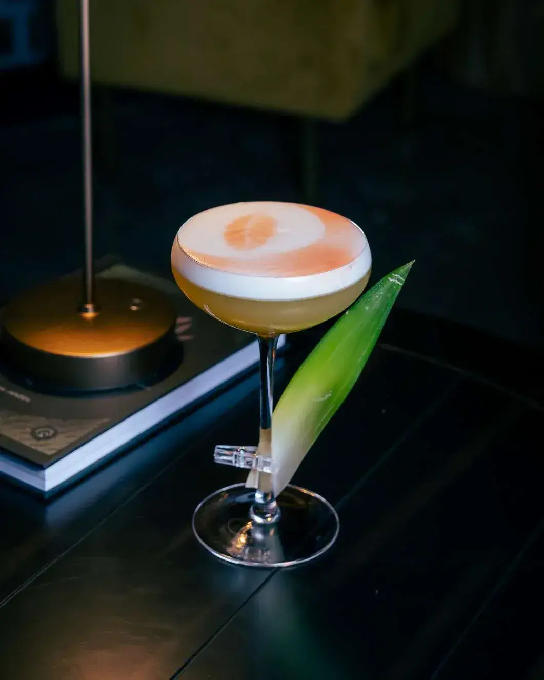 Coupe cocktail with a citrus stencil on the foam and a pineapple leaf garnish