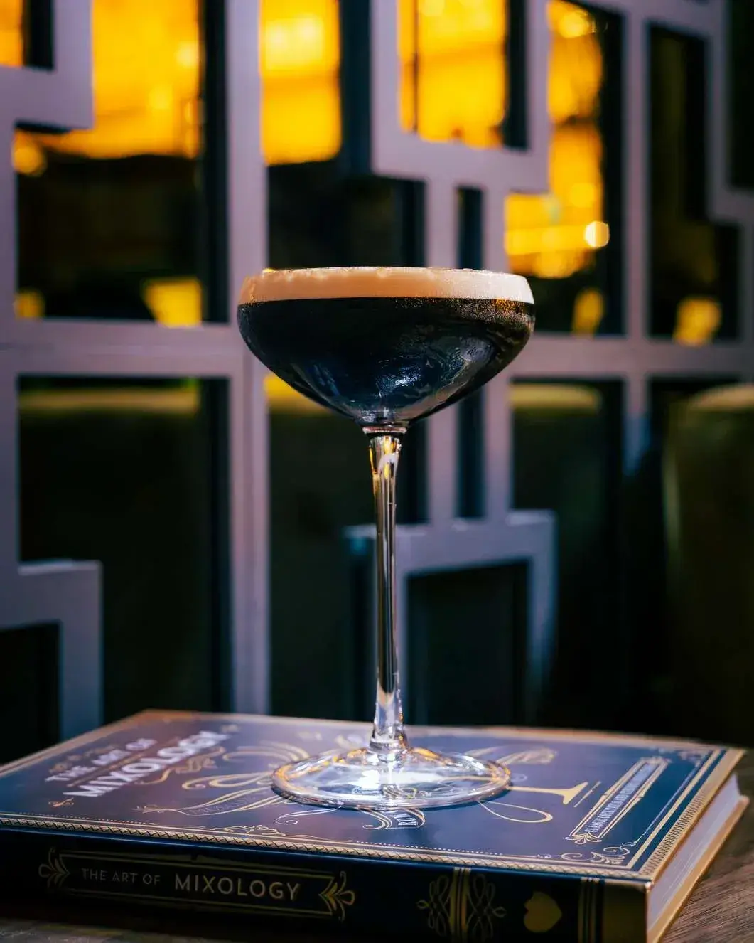 Espresso martini resting on a mixology book in front of the gold lattice screen