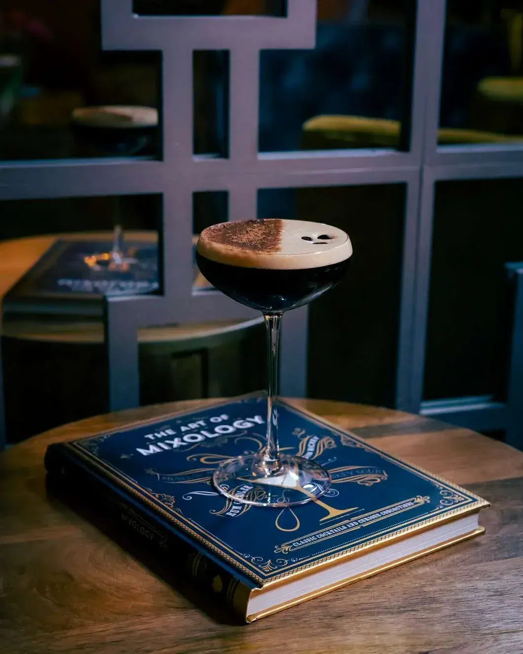 Espresso martini on a mixology book at a wooden table in the lounge