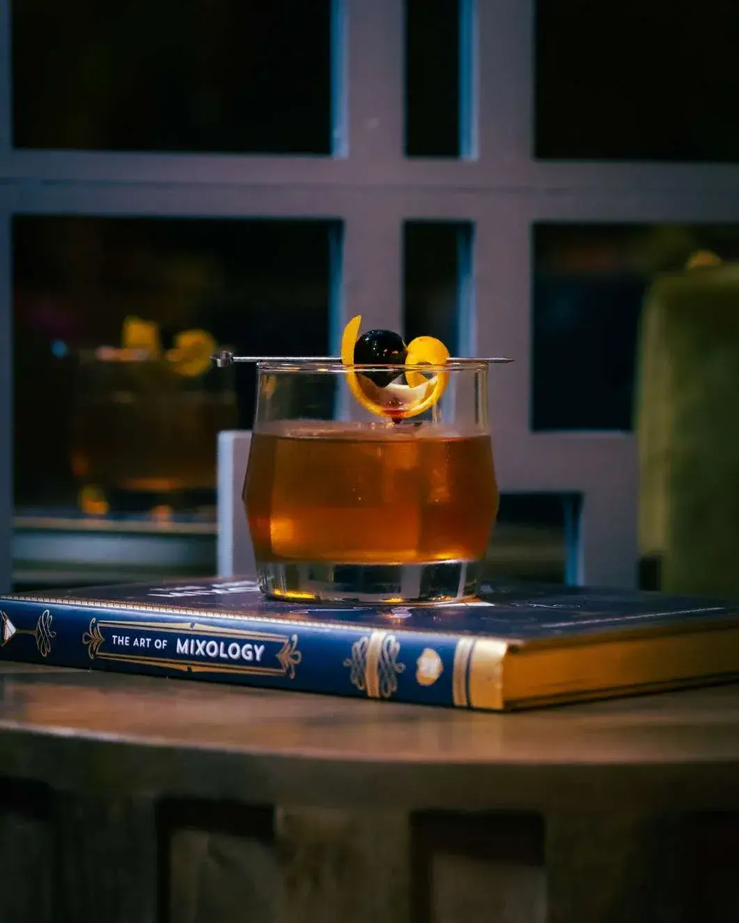 Old fashioned on a mixology book in front of the lattice window screen