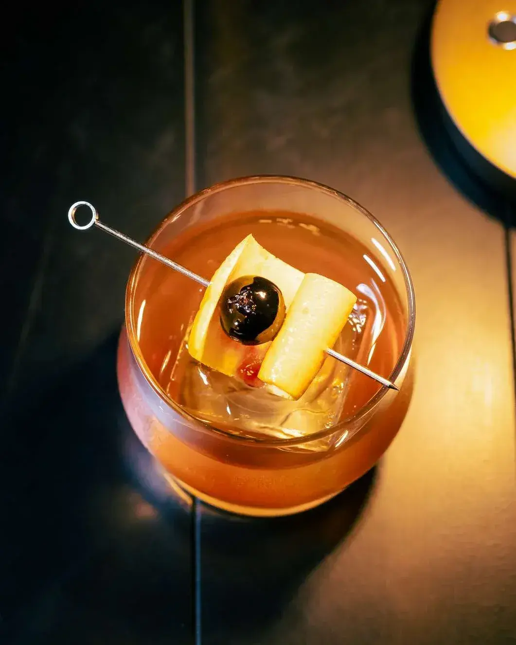 Overhead view of an old fashioned over a clear ice cube, cherry and lemon peel on a pick