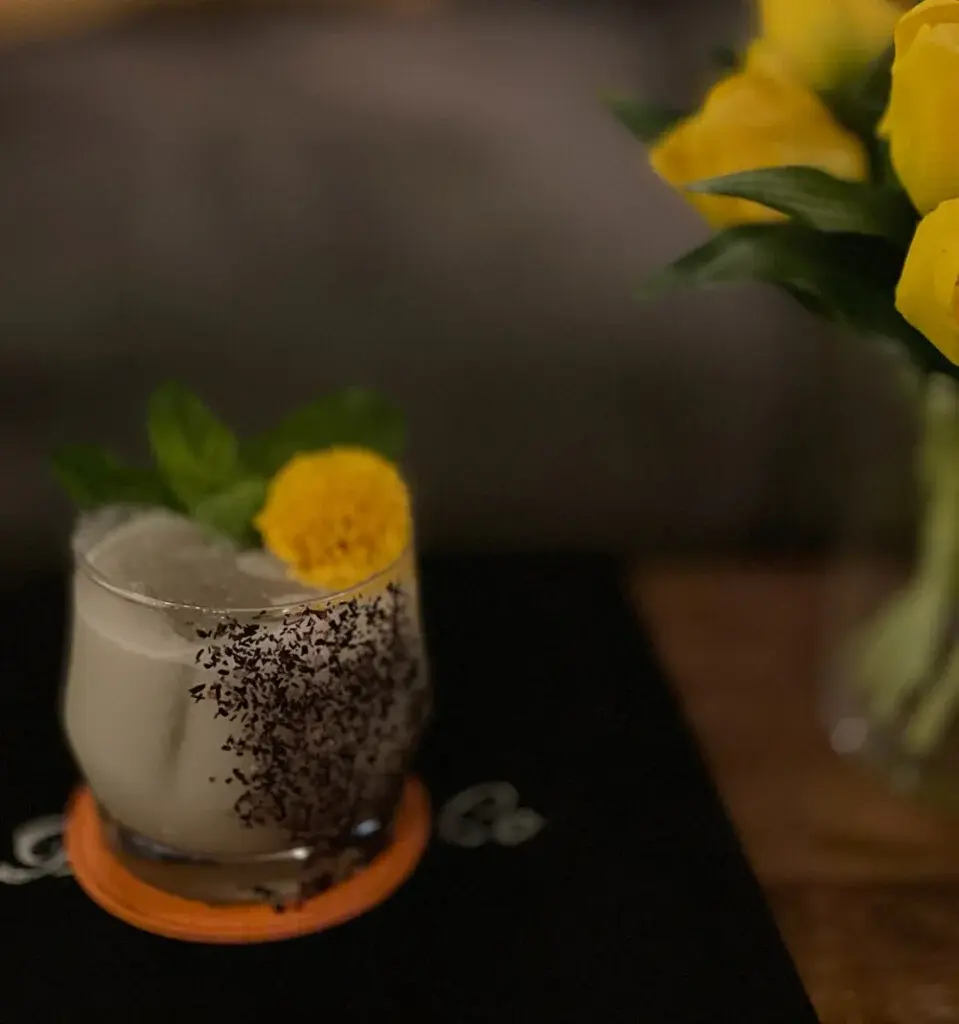 A rocks cocktail with a shaved chocolate rim and marigold