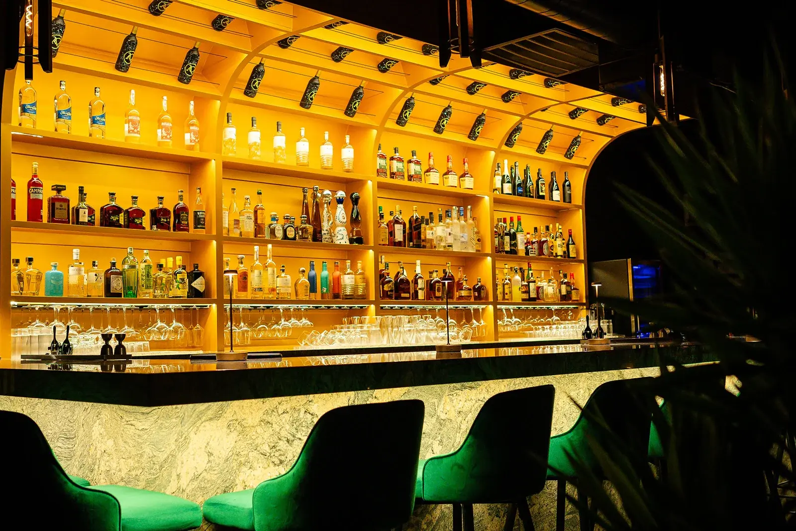 The backlit gold bar at Aye Candy, lined with bottles and green velvet stools