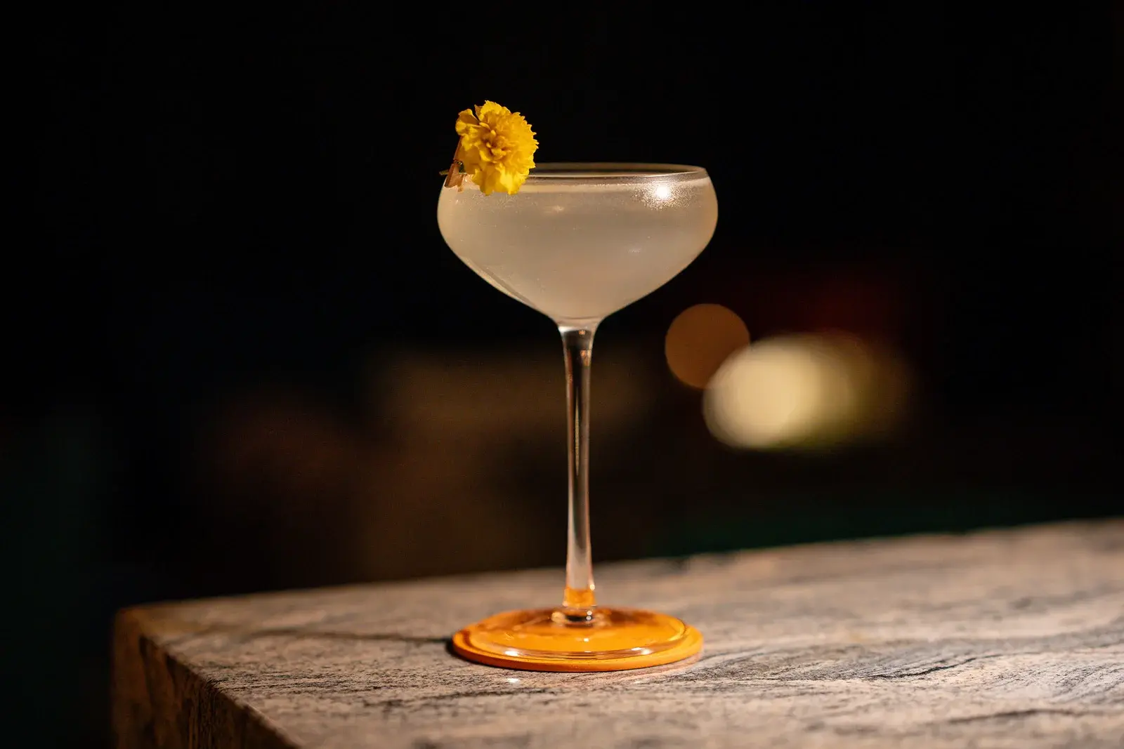 A coupe cocktail garnished with a marigold on the bar top