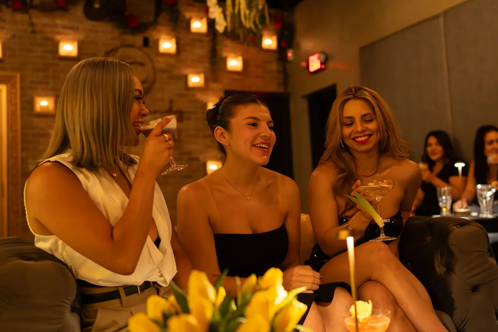 Guests laughing over cocktails in the candlelit lounge at Aye Candy